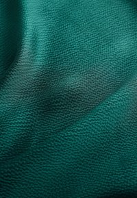 Gros plan sur un tissu texturé vert foncé avec de petits points en relief et des plis doux créant des variations de lumière et d'ombre.