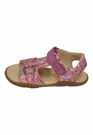 Rosa Kinder-Sandale mit offenem Zehenbereich, weiß gesprenkeltem Muster, verstellbarem Schnallenriemen und Klettverschluss am Knöchel auf einer flachen braunen Sohle.