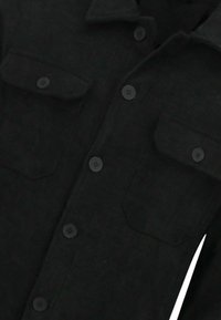 Zwart corduroy overhemd met twee steekzakken aan de voorkant en knoopsluiting. Voorzien van een spitse kraag en een gestructureerde stof.