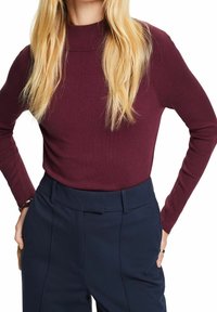 Bordowy prążkowany golf z długim rękawem o dopasowanym kroju, zestawiony z granatowymi spodniami z wysokim stanem, cechującymi się gładką fakturą i eleganckim, dopasowanym wyglądem.