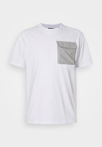 Hvid bomulds T-shirt med en rektangulær grå stoflomme på venstre bryst. Klassisk rund halsudskæring og korte ærmer.