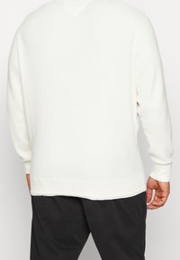 Maglione bianco con texture a waffle, scollo a V, polsini e orlo inferiore a costine. Fit morbido, leggero, cuciture dettagliate lungo le giunture.