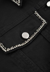 Black denim jacket featuring a studded collar with silver rhinestones and a metal snap button. Close-up view highlighting texture and detailing.
