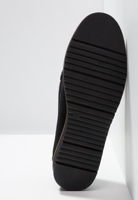 Semelle de chaussure noire avec une surface en caoutchouc texturé, présentant des rainures horizontales et une indication de taille de 37. Dessus en daim doux visible.
