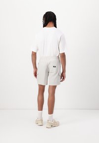 Pantalones cargo gris claro con cintura elástica, dos bolsillos laterales y un bolsillo trasero. Se llevan con una camiseta blanca lisa y zapatillas beige.