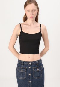 Svart ribbet crop topp med spaghettistropper og logodetaljer, kombinert med et blått denimskjørt med frontknapper og to brystlommer.