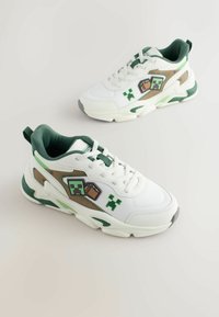 Beli in zeleni supergi z zelenimi in rjavimi igralnimi vzorci v pikslih na strani, prikazani na svetli podlagi.