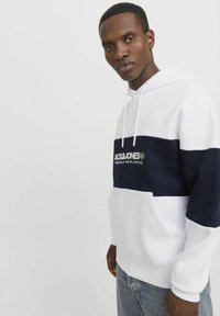 Hætte sweatshirt i hvid og marinblå med et stort centralt stribe og logo. Har ribbede manchetter og kant, samt en frontlomme. Blødt stof.