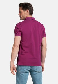 Polo shirt violet avec des manches courtes et des bordures bleu marine sur le col et les manches, associé à un jeans bleu clair. Vu de dos.