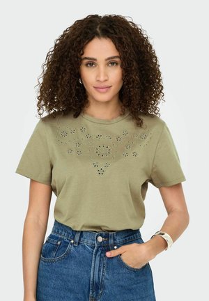 T-shirt verde oliva a maniche corte con dettagli a fiori intagliati sul davanti, abbinato a pantaloni corti in denim a vita alta.