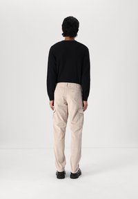 Sort strikket sweater og beige kordfløjl cargo bukser med sidelommer og lige ben design, parret med sorte sko.
