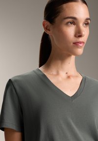 V-kaulust-paita tummanvihreänä, lyhyet hihat, pehmeästä kankaasta valmistettu, jossa on sileä pinta ja rento istuvuus.