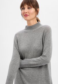 Miękki szary sweter dziany z wysokim, prążkowanym kołnierzem. Posiada długie rękawy i luźny krój, wykonany z teksturowanej, lekkiej tkaniny.