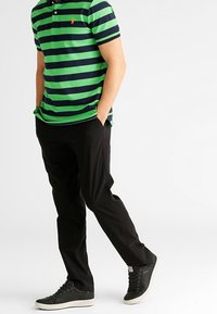 Grön och marinrandig polotröja, svarta byxor och svarta sneakers. Polotröjan har krage och treknappsstängning. Slät bomullstextur.