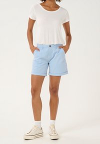 Ljusblå bomullsshorts med uppvikta kanter, med sidofickor och frontknäppning, kombinerade med en vit kortärmad skjorta och sneakers.