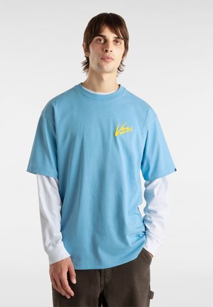 Light blue cotton T-shirt with a round neck, short sleeves, and a yellow Vans logo on the chest, layered over a white long-sleeve shirt.