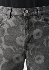Jeans in denim grigio con un delicato motivo floreale nero, design a cinque tasche, chiusura con bottone e dettagli di cucitura visibili.