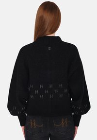 Svart stickad tröja med hög krage och ballongsärmar. Har ett mönster av ljusgrå "H"-symboler över nederkanten. Mjuk textur.