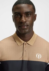Tan og marineblå polo t-shirt med rutemønster, krave og logo på brystet. Har knapper og et tekstureret stof.