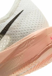 Biegowy but Nike z białą siateczką wierzchnią i czarnym znakiem swoosh, oraz różową gumową podeszwą z fakturowanymi rowkami i wzorami.