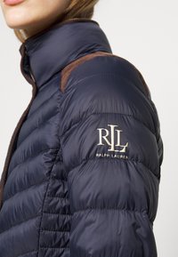 Marineblaue Wattierte Jacke mit gestepptem Muster, braunen Baumwoll-Accessoires an den Schultern und besticktem "RLL"-Logo am Ärmel. Reißverschluss vorne.