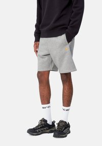 Gray cotton shorts with a side pocket and a small orange logo. Worn with black shoes and white socks featuring black text. Black sweatshirt.
