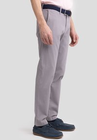 Pantalones de algodón gris con corte recto, combinados con zapatos de ante azul oscuro y un cinturón de fibra trenzada en color marino, mostrados en vista lateral.