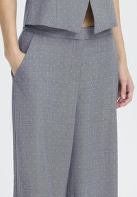 Grå højtaljede bukser lavet af tekstureret stof med små hvide prikmønstre, udstyret med sidelommer og design med vide ben.