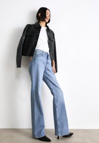 Chaqueta cortada de cuero negro, camisa blanca, vaqueros de pierna ancha azul claro y tacones negros puntiagudos. Texturas suaves, diseño casual, estilo minimalista.