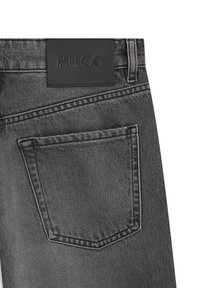 Svarta jeans i denim med en strukturerad yta, utrustade med en bakficka och en läderlapp med logotyp vid midjebandet. Sömmen är i kontrasterande grå färg.