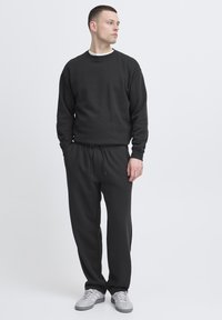 Black sweatshirt and black sweatpants, both with a relaxed fit. Cotton material, crew neck, drawstring waistband, and side pockets.
