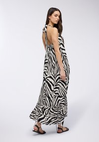 Abito maxi in fantasia zebra bianca e nera, realizzato in tessuto leggero, con orlo a balze e dettaglio con legatura al collo sul retro.