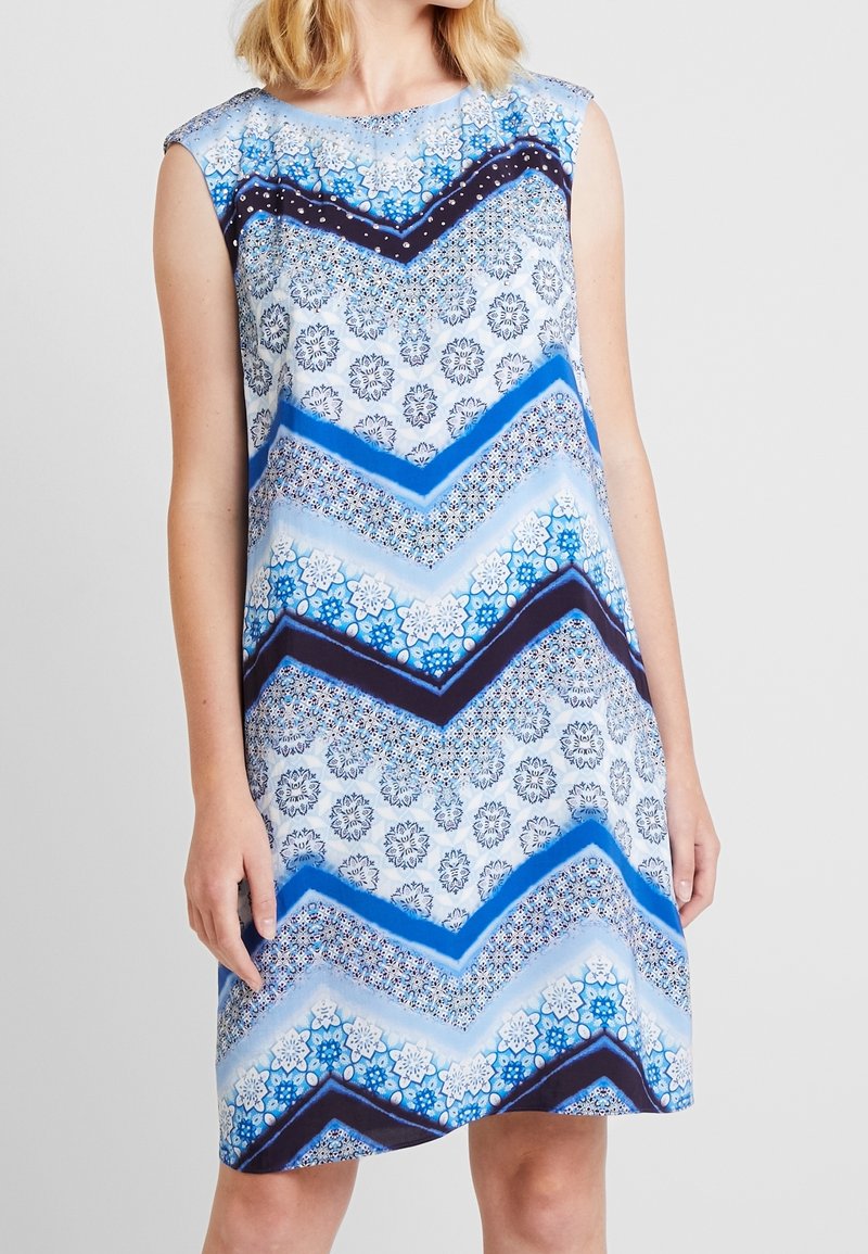 Robe sans manches bleue et blanche présentant des motifs géométriques, des dessins floraux et des accents en chevrons dans des tons bleu foncé et lilas.