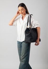 Black leather handbag with structured shape, textured finish, and gold-tone hardware. Model wears a white shirt and blue jeans.