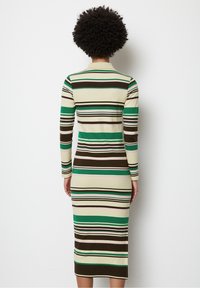 Sukienka z długim rękawem z prążkowanego materiału, z pionowymi paskami w kolorze zielonym, brązowym i kremowym, dopasowana do sylwetki i o długości do połowy łydki.