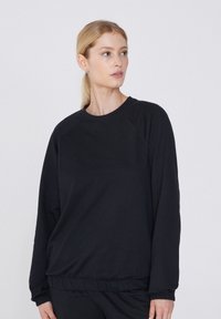 Sudadera negra hecha de tejido suave con cuello redondo, mangas raglán y puños acanalados. Presenta un ajuste holgado y cinturilla elástica.