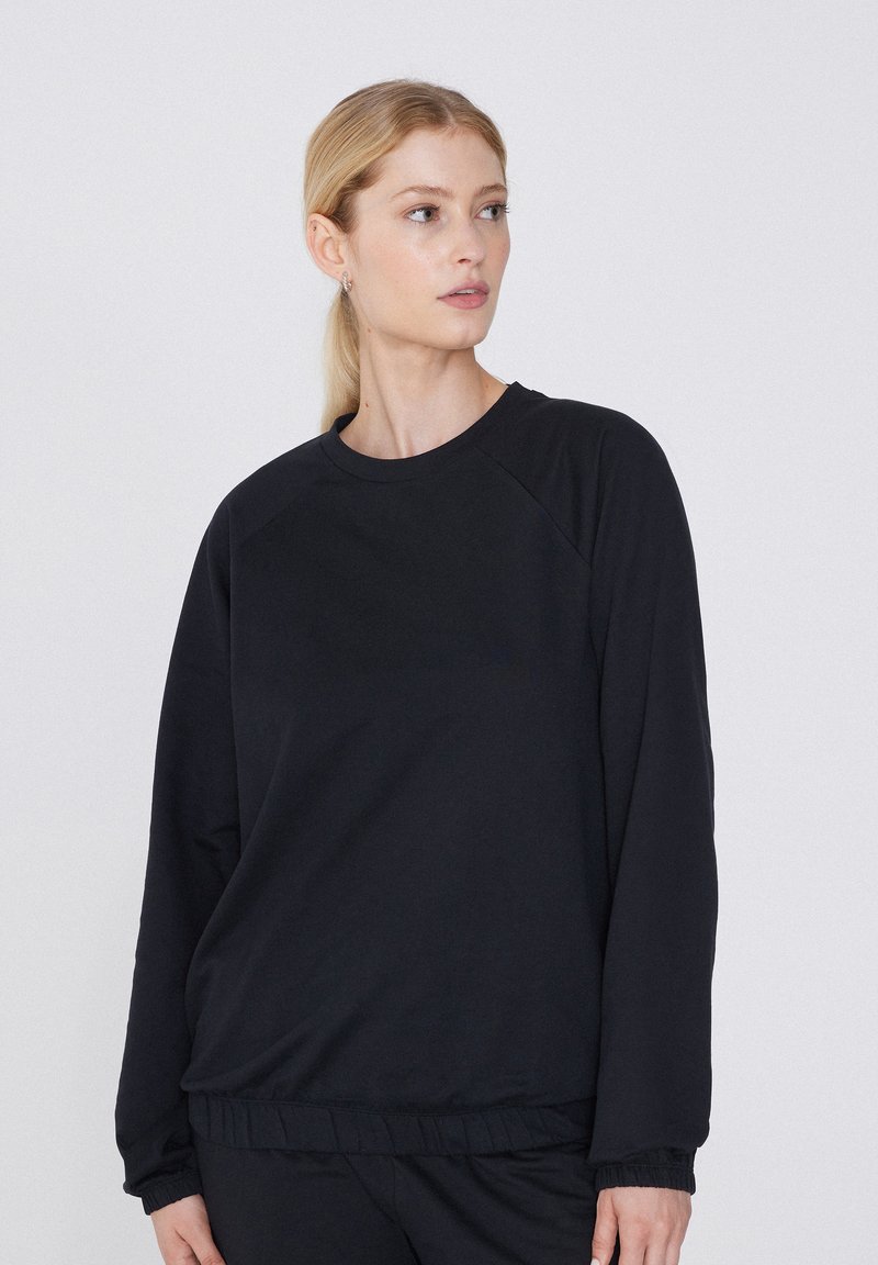 Sudadera negra hecha de tejido suave con cuello redondo, mangas raglán y puños acanalados. Presenta un ajuste holgado y cinturilla elástica.