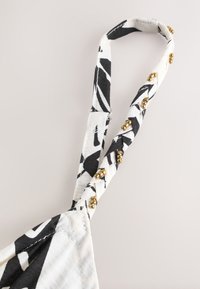 Sangle en tissu à motif noir et blanc torsadée avec de petites perles dorées cousues tout le long sur un fond clair.