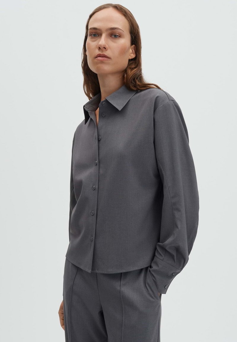 Chemise grise boutonnée avec un col classique, des manches longues et une texture lisse. Présente des détails de boutons subtils et une coupe ajustée.