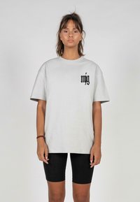 Light gray oversized t-shirt with short sleeves and a rounded neckline featuring black text on the left chest area, paired with black bike shorts.