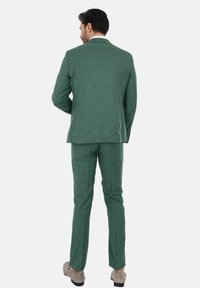 Completo da uomo a due pezzi in tessuto verde testurizzato. Presenta un design su misura con una fessura singola sul retro ed è abbinato a pantaloni coordinati.