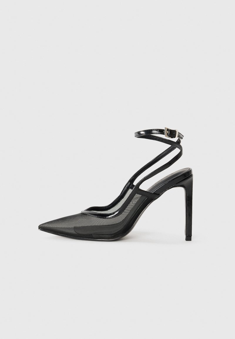 Escarpins noirs à talon haut avec un bout pointu, une combinaison de mesh et de cuir verni, un strap au niveau de la cheville avec une boucle, silhouette élégante.