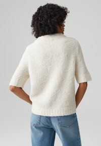 Maglione bianco, tessuto a trama, con maniche corte, scollo rotondo e vestibilità rilassata, abbinato a jeans in denim azzurro chiaro.