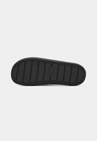 Semelle de chaussure en caoutchouc noire avec des lignes de rainures horizontales et une petite marque rectangulaire au centre sur fond blanc.
