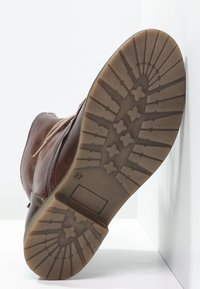 Braune Lederstiefel mit einer strukturierten Gummisohle. Das Profil hat ein gemustertes Design mit einem seitlichen Etikett, das "37" beschriftet ist. Zeigt eine flache Silhouette.