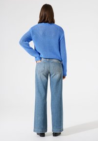 Blauer, gestrickter Pullover mit lockerer Webart, kombiniert mit weit geschnittenen, hellblauen Jeans. Einfaches Design mit Gesäßtaschen an den Jeans.