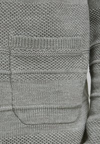 Maglione grigio chiaro lavorato a maglia con motivi testurizzati, taschino sul petto e dettagli a costine sui polsini e sull'orlo. Materiale morbido e traspirante.