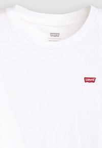 Weißes Baumwoll-T-Shirt mit Rundhalsausschnitt und kleinem roten Levi's-Logo-Patch auf der linken Brust. Glatte Textur, schlichtes Design.