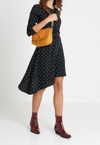 Černé šaty s bílými puntíky, asymetrický lem, spárované se žlutou kabelkou přes rameno a bordó kotníkovými botami s nízkým podpatkem.