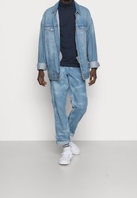 Ljusblå jeansjacka, kombinerad med en marinblå rullkrage och matchande ljusblå jeans. Vita sneakers med svarta randiga strumpor.